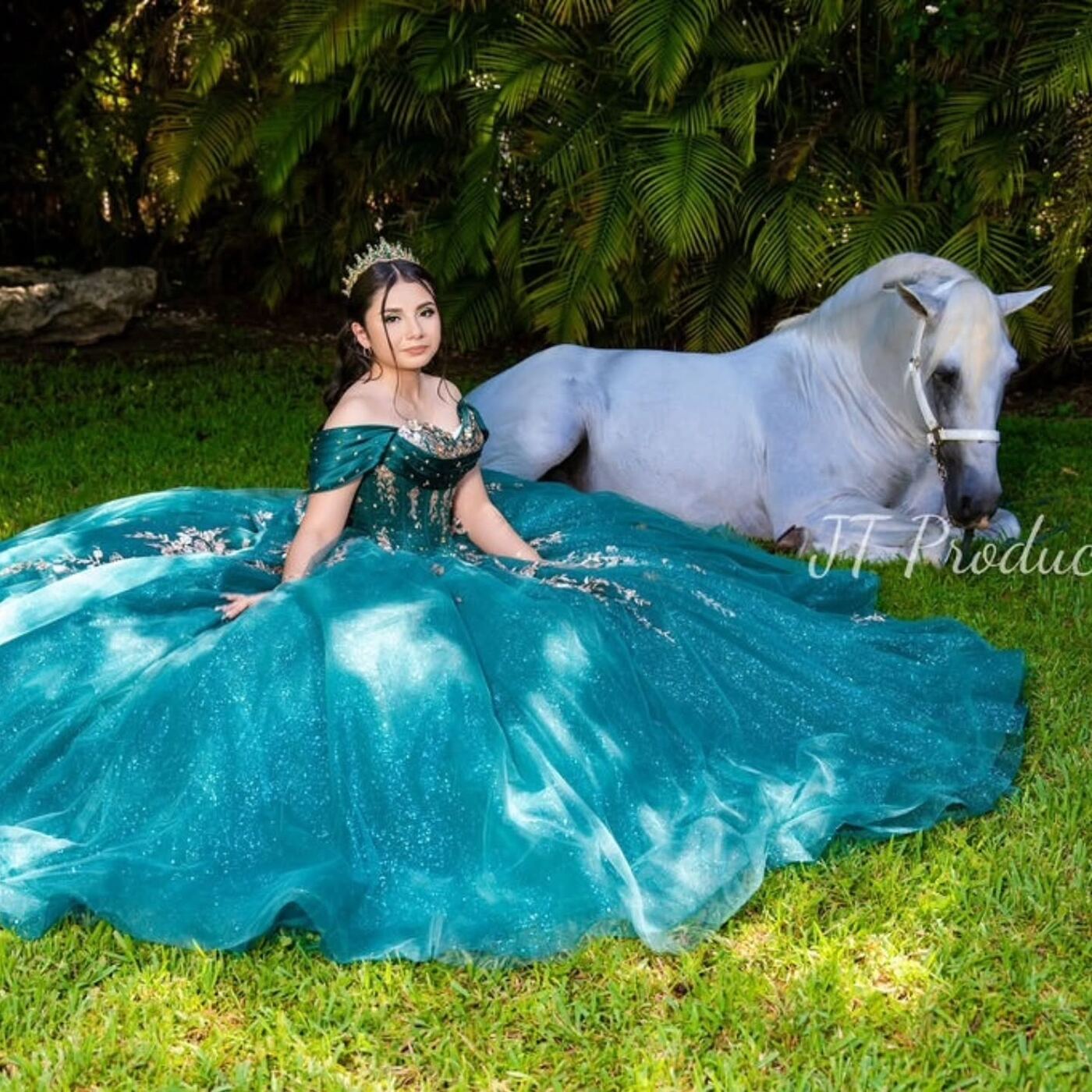 Quinceañera con vestido verde junto a un caballo blanco recostado