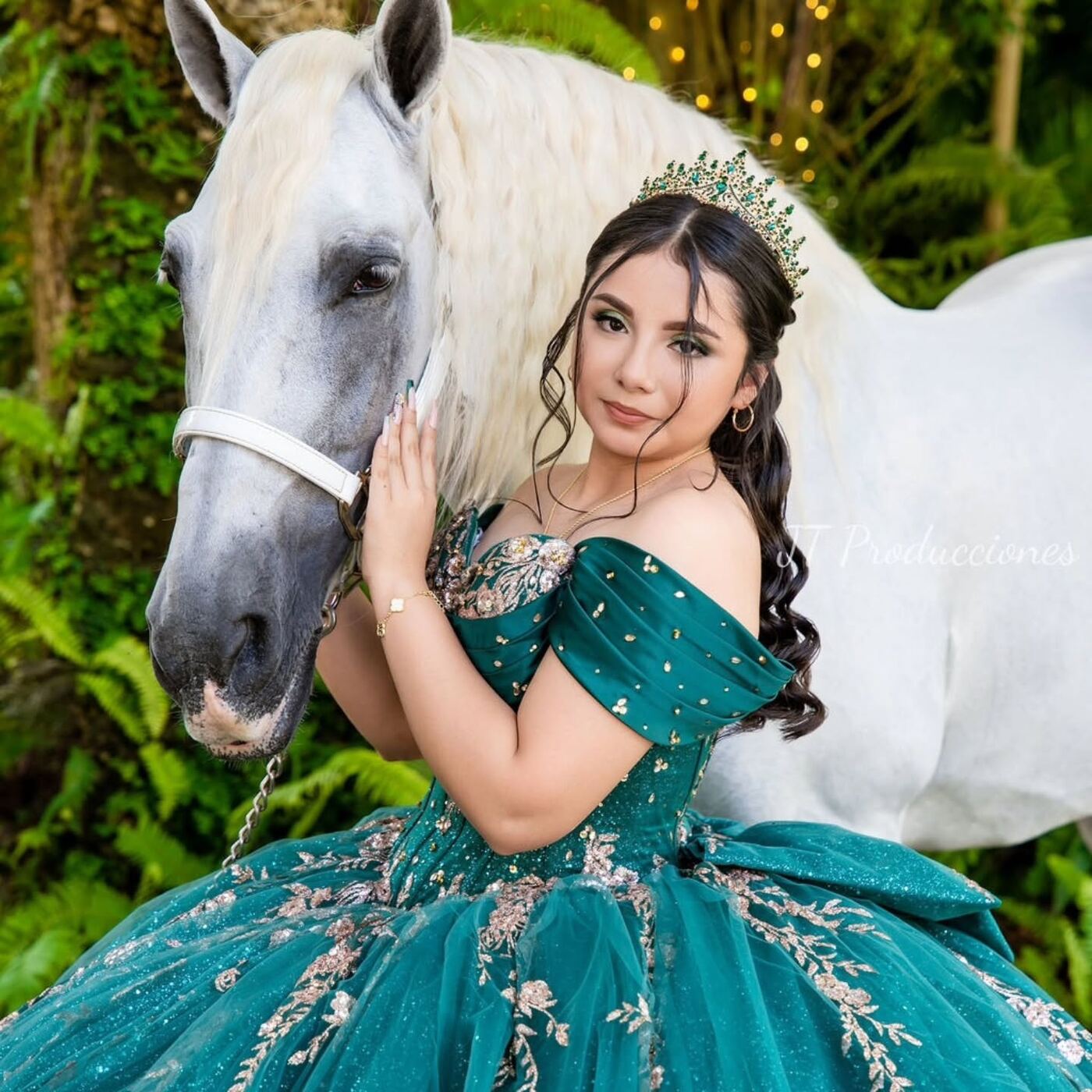 Quinceañera con vestido verde esmeralda junto a un caballo blanco